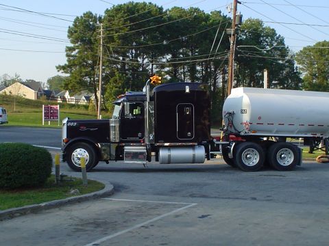 1966 International School Bus - A black semi-truck with a white tanker trailer is parked on a paved surface.
