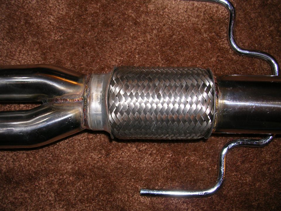 Exhaust pipe with braided flex section and chrome hangers against brown carpet