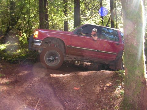 1991 Ford Explorer - Red SUV navigating a wooded trail with steep inclines and loose dirt.