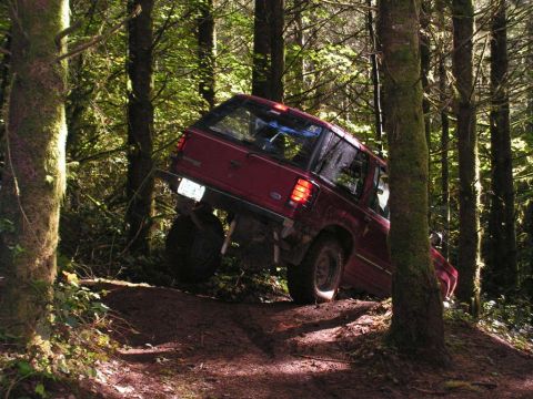 1991 Ford Explorer - This red 1991 Ford Explorer navigates a challenging off-road trail surrounded by dense forest.