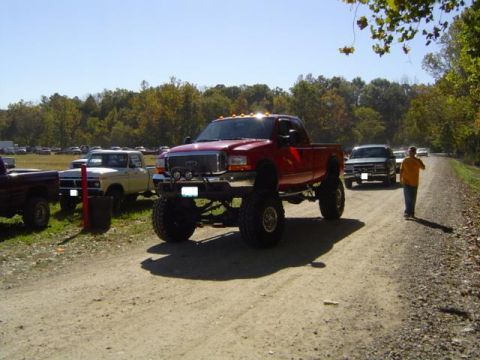1979 Ford Bronco - Several trucks are parked and driving on a dirt road during an outdoor event.