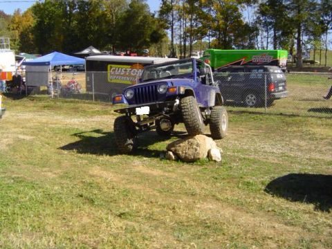 1979 Ford Bronco - A blue Jeep Wrangler is shown navigating an off-road course, with its tires on a large rock.
