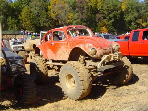 1979 Ford Bronco - Modified Volkswagen Beetle at a mud bogging event, surrounded by other off-road vehicles.