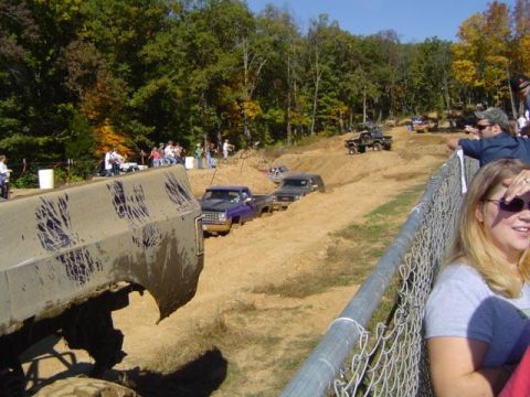 1979 Ford Bronco - Multiple trucks navigate a muddy off-road course during an event with onlookers.