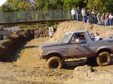 1979 Ford Bronco - Ford Bronco navigates a challenging mud course with onlookers watching from the embankment.