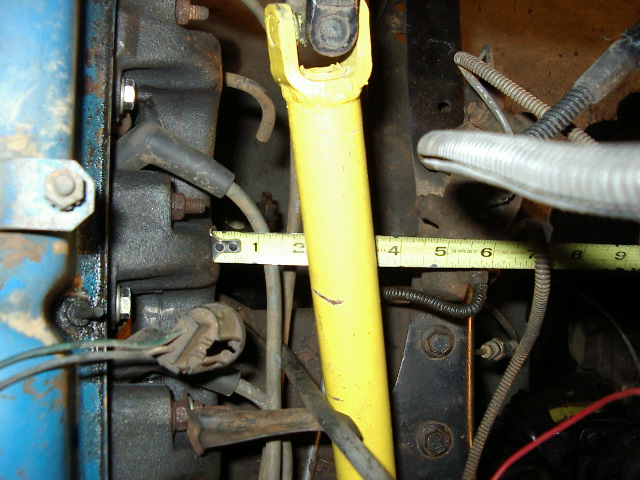 Close-up of engine bay components with a yellow measuring tape extended across part of the engine block and a yellow driveshaft