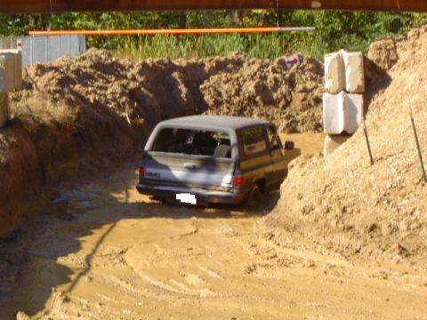 1979 Ford Bronco - A GMC SUV navigates a muddy obstacle course, its rear end visible as it gets stuck.