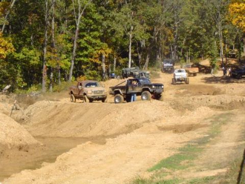 1979 Ford Bronco - Multiple off-road vehicles participate in a mud bash event on a sunny day with autumn foliage.