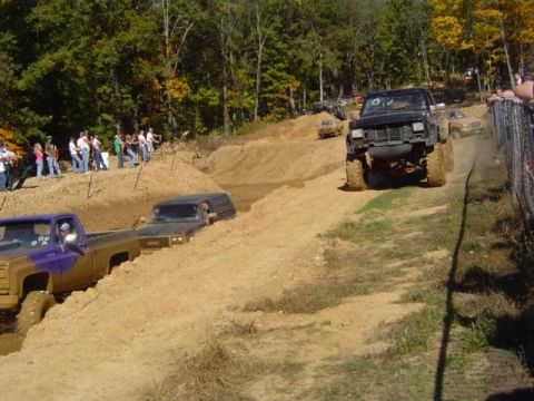 1979 Ford Bronco - Multiple off-road vehicles are seen participating in a mud bog event with spectators lining the course.