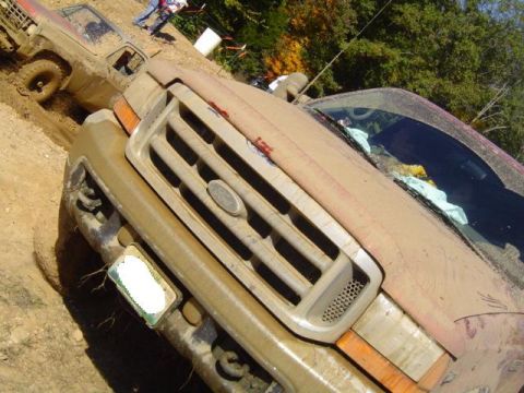 1979 Ford Bronco - A muddy Ford truck's grille is the focus, with another off-road vehicle partially visible in the background during an event.