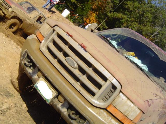 Mud-covered Ford truck grille, front view. Another muddy vehicle is visible behind