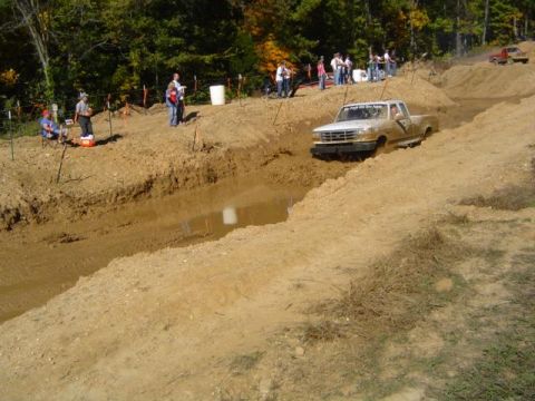 1979 Ford Bronco - A white pickup truck navigates a muddy obstacle course with spectators watching.