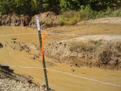 1979 Ford Bronco - A muddy track with a barbed wire fence and an orange marker in the foreground.