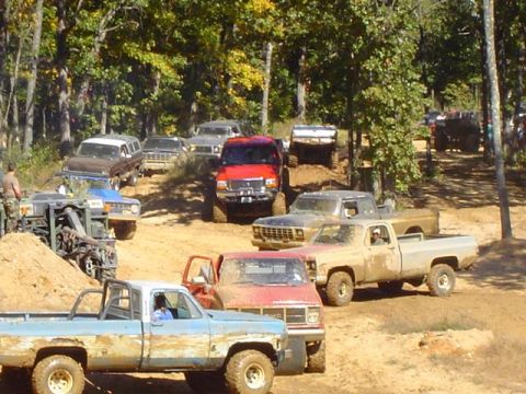 1979 Ford Bronco - A group of off-road vehicles are gathered in a wooded area, with some driving and others parked.