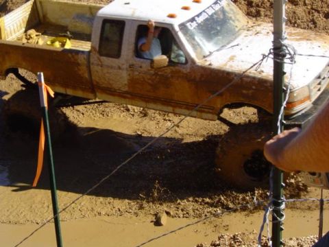 1979 Ford Bronco - A pickup truck is stuck in the mud during an event, with a person visible inside the cab.