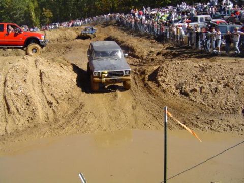 1979 Ford Bronco - A 1979 Ford Bronco tackles a challenging mud pit during an off-road event, with a crowd gathered to watch the side.