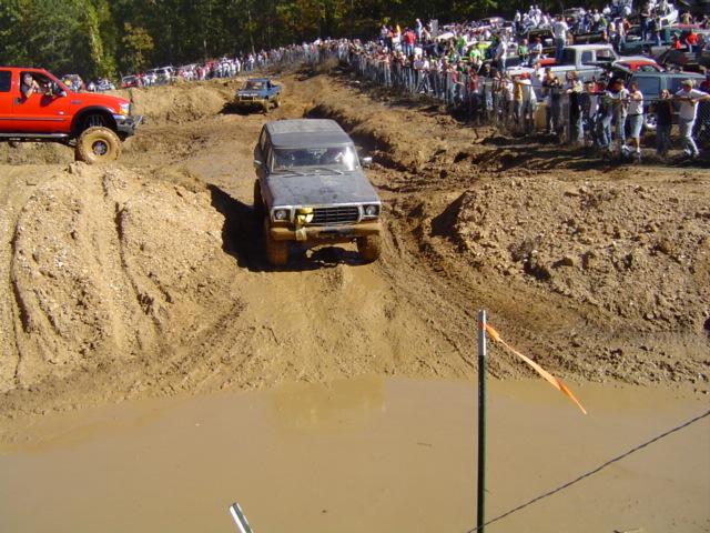 Gray 1979 Ford Bronco navigating a muddy obstacle course with spectators watching