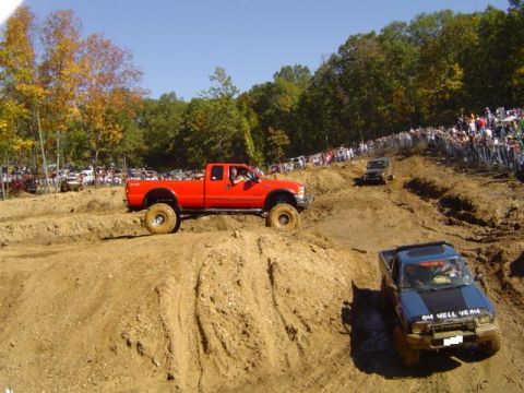 1979 Ford Bronco - Multiple trucks navigate a muddy off-road course with spectators lining the hills.