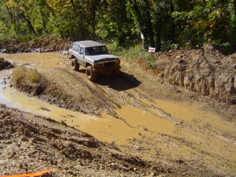 1979 Ford Bronco - A 1979 Ford Bronco navigates a challenging muddy terrain with deep ruts and water.