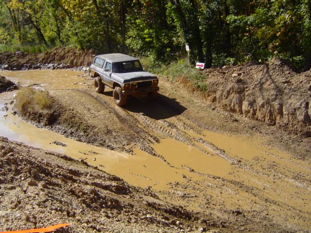 Gray 1979 Ford Bronco driving through a muddy off-road course