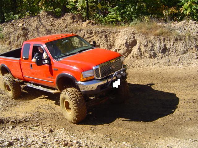 Orange Ford F-250 Super Duty pickup truck with large tires driving on a muddy dirt road