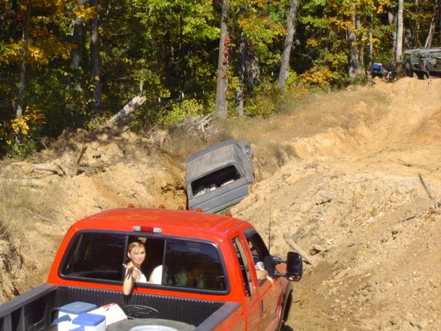 Red pickup truck and a gray SUV on a dirt hill with trees in the background
