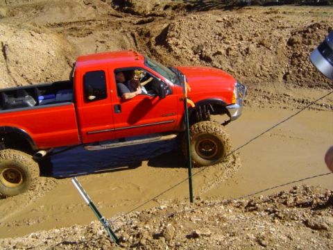 1979 Ford Bronco - A red pickup truck navigates a muddy obstacle course during an event.