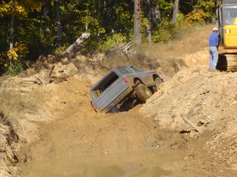 1979 Ford Bronco - A pickup truck is stuck in a muddy pit while an excavator stands on the bank.