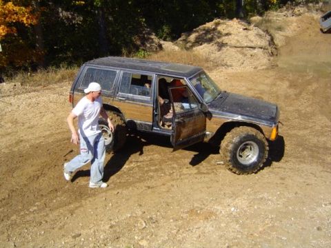 1979 Ford Bronco - A black SUV with wood paneling is seen off-roading with its door open, while another vehicle is visible in the background.