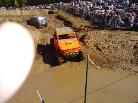1979 Ford Bronco - Off-road vehicles tackle a muddy course with a crowd gathered to watch the event.