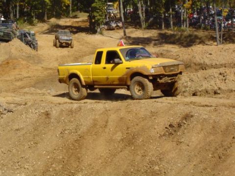 1979 Ford Bronco - A yellow pickup truck navigates a muddy off-road course during a daytime event.