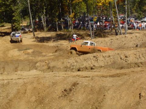 1979 Ford Bronco - An orange pickup truck navigates a muddy obstacle course, with onlookers gathered to watch the event.