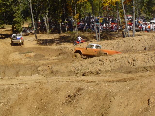 Orange pickup truck stuck in mud pit with spectators in background