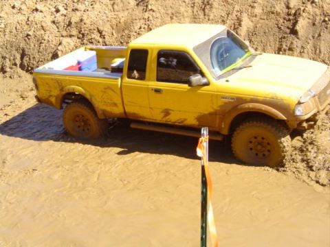 1979 Ford Bronco - A yellow pickup truck is stuck in deep mud, with its tires partially submerged.