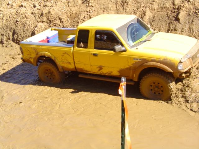 Yellow pickup truck with mud splattered all over it, stuck in a muddy ditch