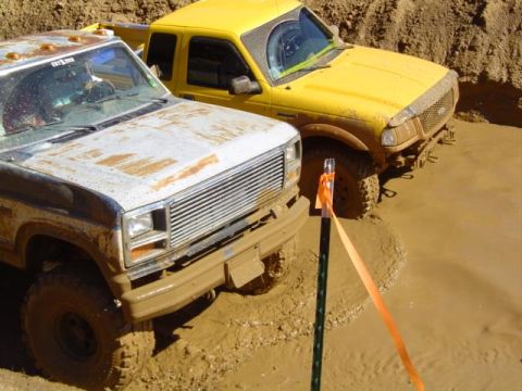 1979 Ford Bronco - Two trucks are stuck in a mud pit, with the front of a white truck visible next to a yellow truck.