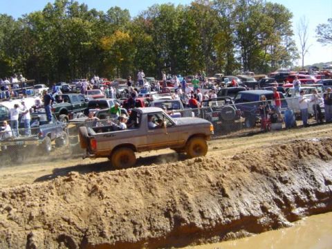 1979 Ford Bronco - A 1979 Ford Bronco navigates a muddy track during an event, with a crowd gathered to watch.