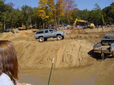 1979 Ford Bronco - Mud bogging event features several trucks and an excavator on a sunny day.