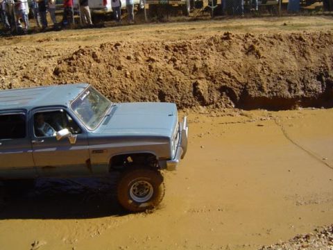 1979 Ford Bronco - A light blue SUV navigates a muddy terrain during an event.