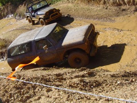 1979 Ford Bronco - Two off-road vehicles navigate a muddy terrain, with one SUV deeply stuck in the mire.