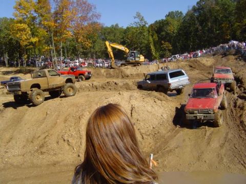 1979 Ford Bronco - Multiple off-road vehicles tackle a challenging mud course during an event, with a crowd watching and construction equipment nearby.