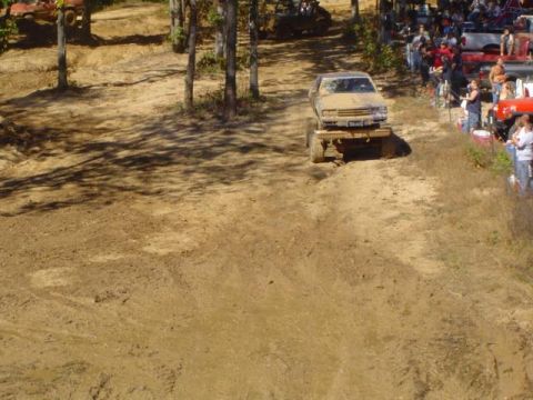 1979 Ford Bronco - A heavily modified pickup truck navigates a muddy hill during an off-road event with onlookers present.
