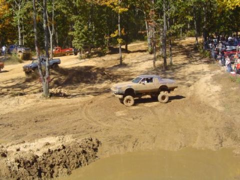 1979 Ford Bronco - A lifted car navigates a muddy course during an event with spectators watching.