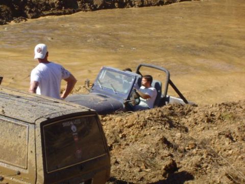 1979 Ford Bronco - Two off-road vehicles are stuck in a muddy pit during an event.