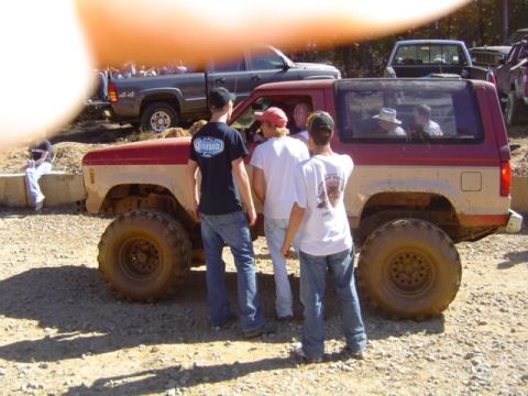 1979 Ford Bronco - A group of people stand around a lifted, two-tone SUV with oversized tires at an outdoor event.