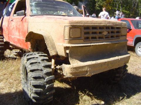 1979 Ford Bronco - Muddy pickup truck with oversized tires at an outdoor event. Another vehicle is parked nearby.