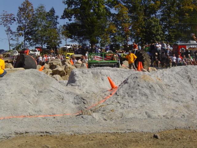 Off-road vehicles and spectators gathered at a dirt and rock obstacle course