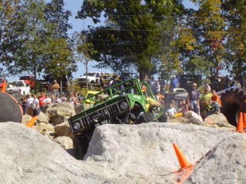 1979 Ford Bronco - A green off-road vehicle tackles a rocky obstacle course with spectators gathered around.
