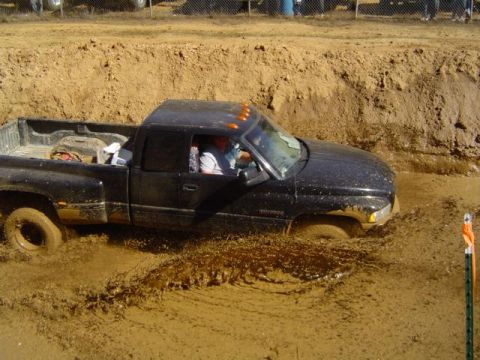 1979 Ford Bronco - A black pickup truck is stuck in a muddy pit, with water splashing around it.
