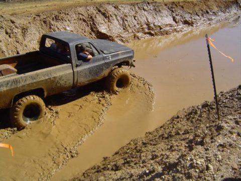 1979 Ford Bronco - A black pickup truck navigates a deep mud pit during an off-road event.